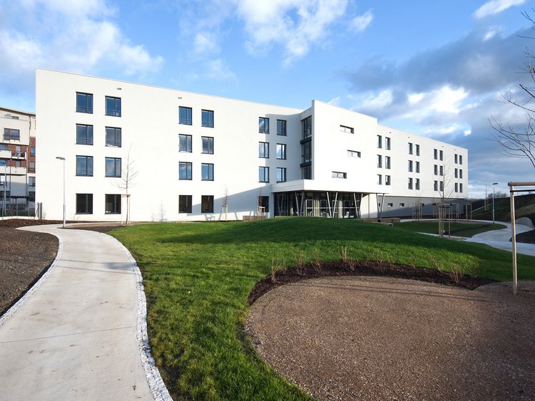 Photo: building with white façade; garden areas and paths in the foreground