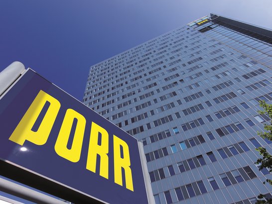 Mrakodrap pod modrou oblohou s modrým logem PORR v popředí