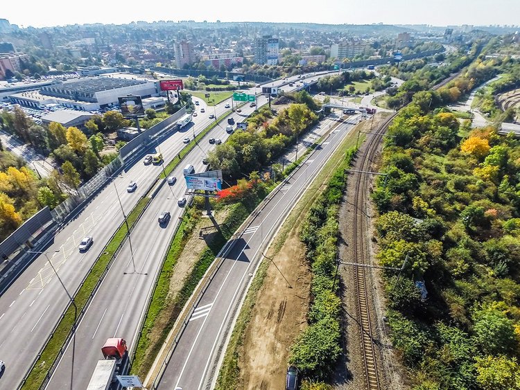 Photo: aerial view of a multi-lane road; on the right, the new exit; further right, a railway line among trees; large city in the background