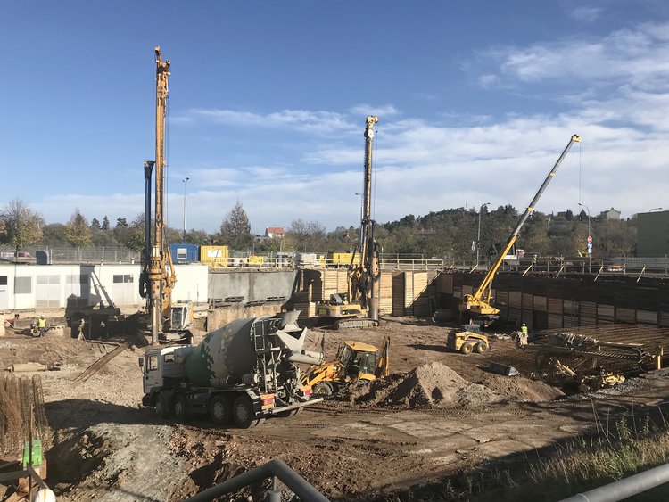 Photo: Construction site with foundation work in progress, three yellow construction machines in the background and yellow excavator with the concrete mixer in the foreground